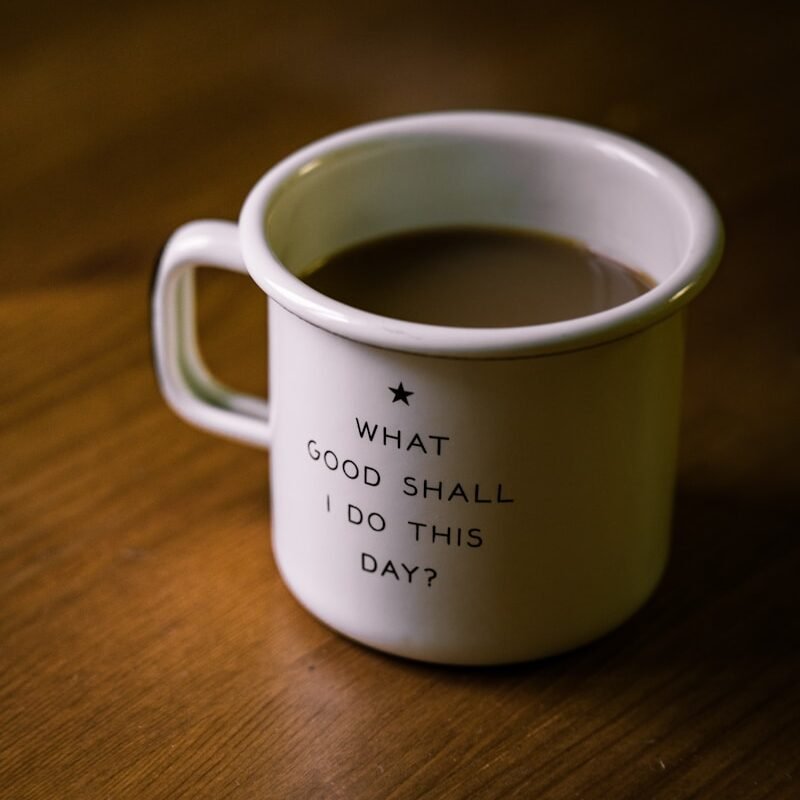 white and black ceramic cup filled with brown liquid on brown wooden sufface